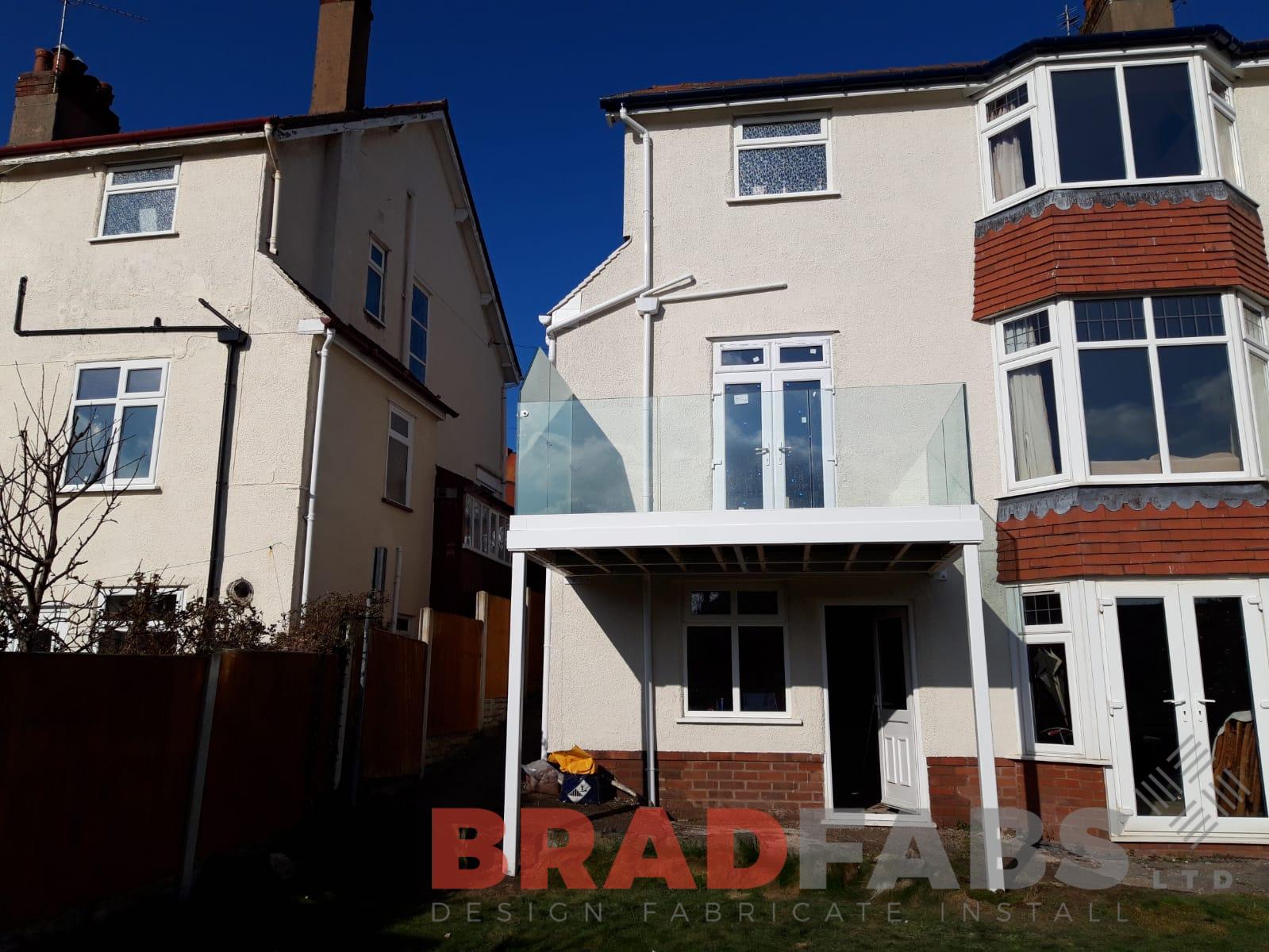 Mild steel, galvanised and powder coated balcony with supporting legs by Bradfabs. Channel system infinity glass balustrade with privacy screen to one side. Complete with composite decked flooring 