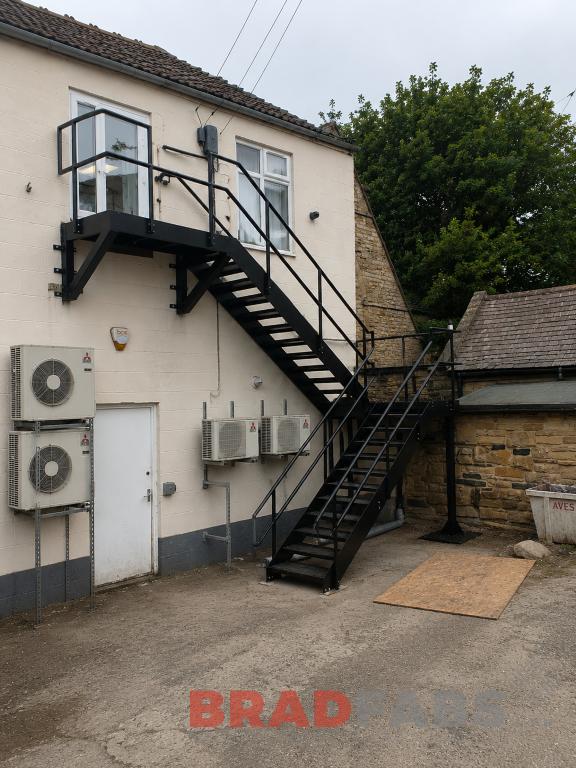 External black powder coated steel fire escape staircase with intermediate landing and access platform installed on a commercial building in Pudsey